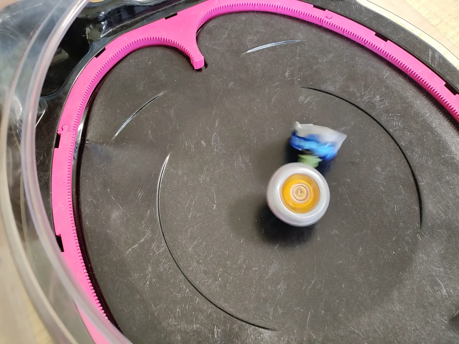 決着の瞬間。銀×オレンジのベイが回り続け、青×白が弾かれて傾く