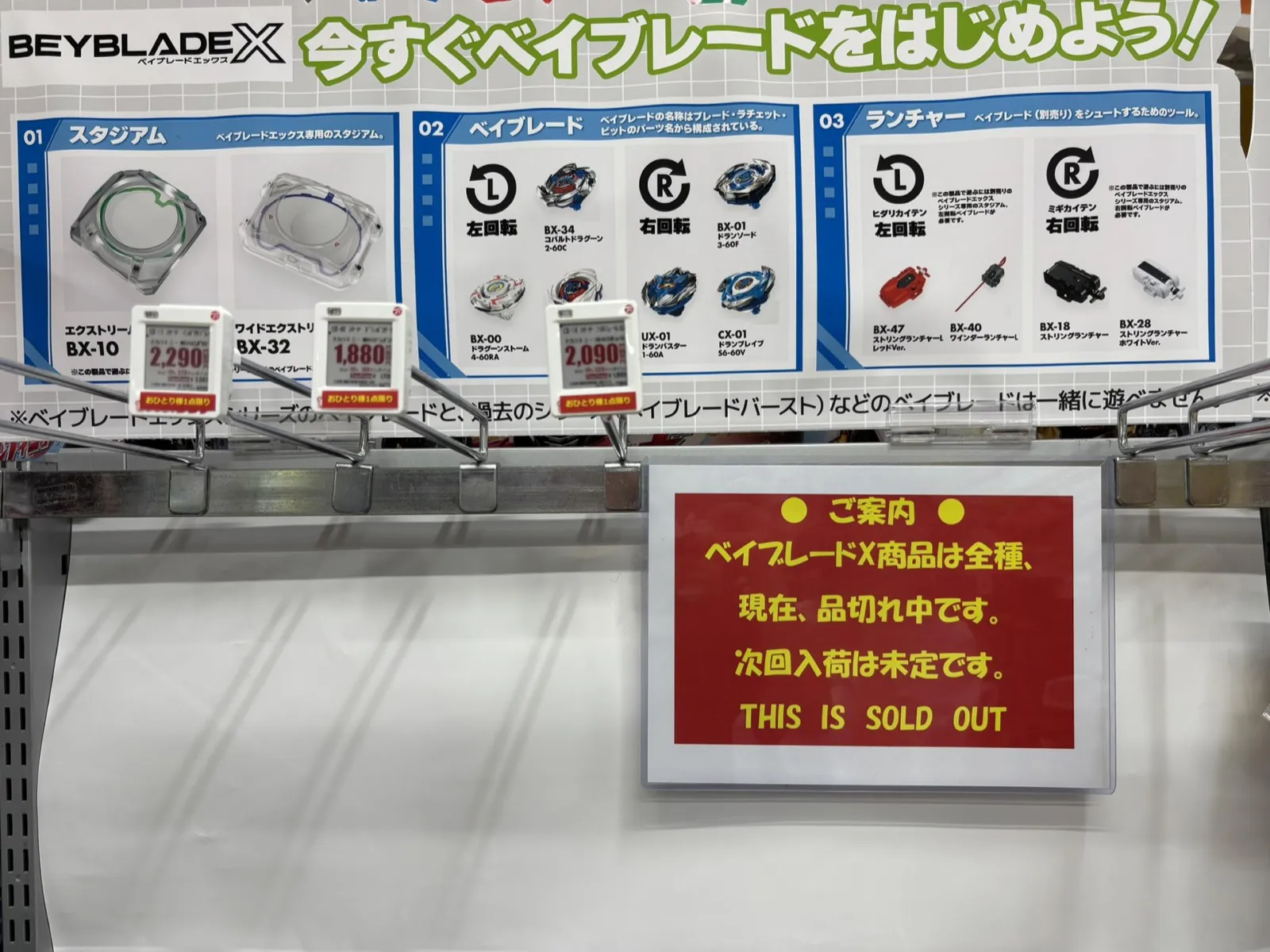 量販店のベイブレードX売り場に貼られた「全種品切れ・次回入荷未定」の案内と空いた棚